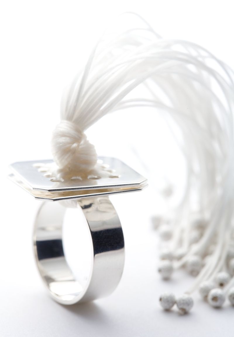 Medusa Ring. Material: Silber, Gummischnüre weiß. Silberring mit zwei quadratischen Plättchen, durch die viele braune Gummischnüre gezogen sind und die in einem tentakelartigen Schweif auslaufen.