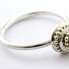 Törtchenförmiger Ring und mit einem 14kt goldenen Kugeldraht versehen.  In der Mitte ist erhaben ein facettierter, weißer Zirkon gefasst.