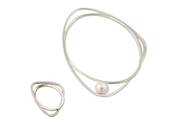 Armreif aus Silber mit Süßwasserperle und passender Ring. Die Form besteht aus zwei ineinander verschlungenen Elementen, einem ovalen und einem gerundet-dreieckigen.