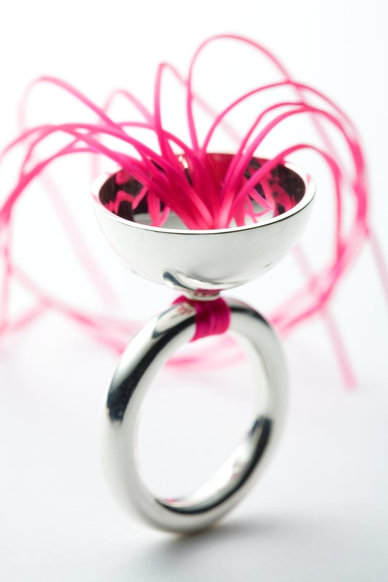 Medusa Ring. Material: Silber, Gummischnüre pink. Silberring mit einer Halbkugel oben, durch die viele braune Gummischnüre gezogen sind und die in einem tentakelartigen Schweif auslaufen.
