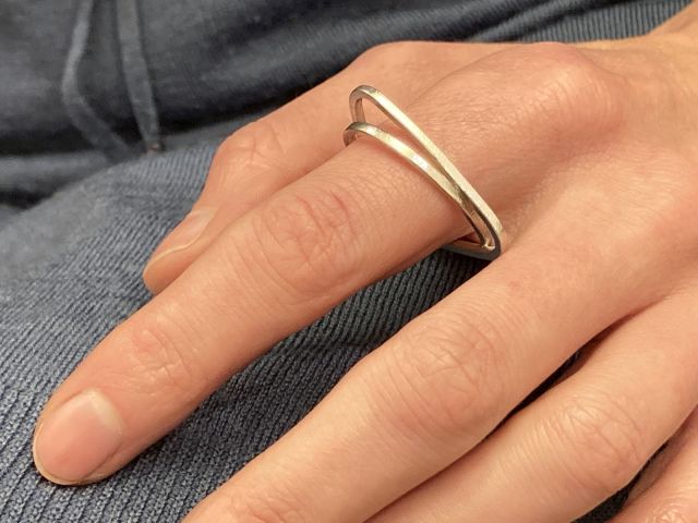 Ein ovaler und ein gerundet-dreieckiger Ring,  ineinander verschlungen aus vierkantigem Silberdraht, getragen.