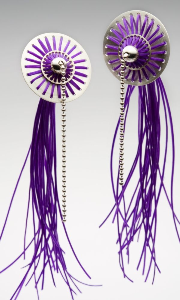 Medusa Ohrringe. Material: Silber, Gummischnüre violett. Der scheibenförmige Körper dieser leichten Ohrringe wird von vielen, rund angeordneten Gummischnüren überspannt, die in einem tentakelartigen Schweif auslaufen.